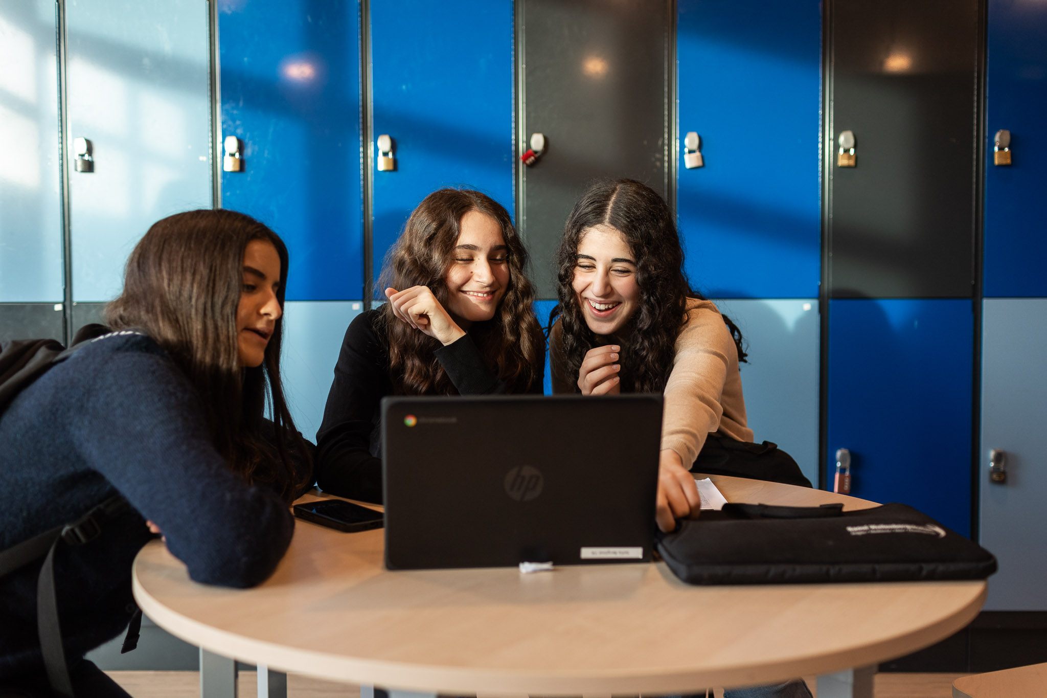 3 elever som sitter tillsammans vid en dator i skolkorridoren.